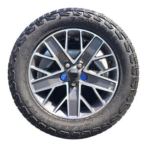 以下が含まれることがあります： 黒とシルバーの車のホイールのクローズアップ。頑丈なタイヤが付いています。ホイールは、青いセンターキャップが付いたマルチスポークデザインです。タイヤの側面には「GRABBER」の文字があります。