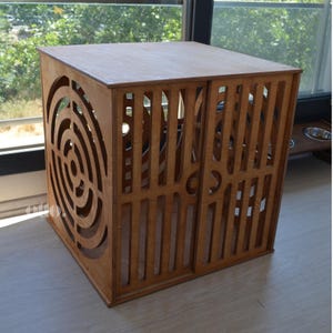 May include: A wooden pet crate with a circular cutout design on one side and a slatted door on the other side. The crate is made of natural wood and has a light brown finish.