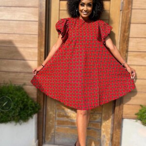May include: A red and black patterned dress with short puff sleeves. The dress has a loose fit and falls to the knees. The model is wearing black heeled sandals.