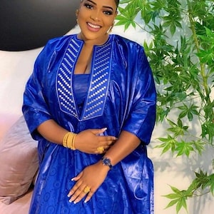 May include: A woman wearing a blue and silver embroidered dress with a V-neckline. She is wearing gold jewelry and a watch.