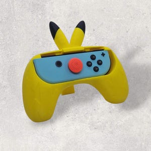 May include: A yellow controller grip with black-tipped ears, designed to resemble a popular cartoon character. The controller holds a blue game console with black buttons and a red button. The grip has a textured surface and is designed for gaming.