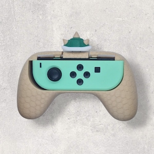 Può includere: Un'impugnatura personalizzata per controller Joy-Con Nintendo Switch beige e verde acqua. L'impugnatura ha un motivo strutturato e un design a guscio di Bowser sulla parte superiore. Il Joy-Con è verde acqua con pulsanti neri.