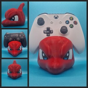 May include: A red and white 3D printed video game controller stand shaped like a cartoon dragon's head. The stand is designed to hold a white Xbox controller.