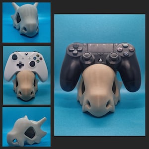 May include: A 3D printed grey and white Pokemon skull-shaped stand for a black Playstation 4 controller.