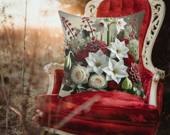 May include: A white and red floral pillow with a variety of flowers, including white roses, red roses, and white lilies. The pillow is sitting on a red velvet chair.