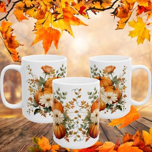 May include: Three white ceramic mugs with a fall-themed design featuring pumpkins, flowers, and leaves. The mugs are arranged in a row on a wooden surface with fall leaves scattered around them.