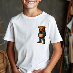 May include: White t-shirt featuring a cartoon bear wearing sunglasses, a hoodie with an American flag design, and jeans. The bear is standing with its hands in its pockets. The shirt is a classic crew neck.
