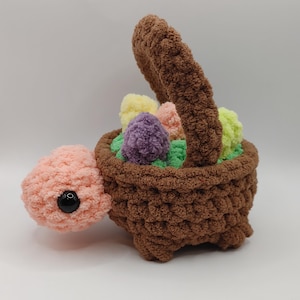 May include: A handmade crochet Easter basket shaped like a turtle, with a brown basket and handle, a peach-colored head, and a black eye. The basket is filled with colorful, fluffy eggs in shades of yellow, pink, purple, and green.