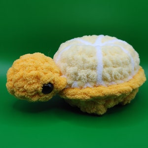 May include: A crocheted stuffed turtle toy with a yellow head and legs and a white shell with a yellow border.
