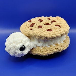 May include: A crocheted stuffed toy shaped like an ice cream sandwich. The top and bottom cookies are brown with chocolate chips and the ice cream filling is white.