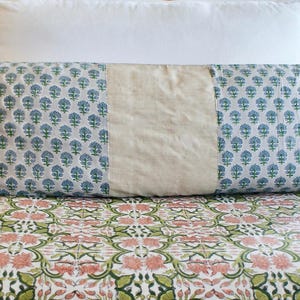 May include: A long rectangular pillow with a white background and a blue floral pattern. The pillow has a beige fabric panel in the center.