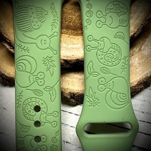 May include: A light green silicone watch band featuring an engraved pattern of various snails, leaves, and small sprigs. The design is repeated across the surface of the two band segments, which include standard attachment slots and adjustment holes.