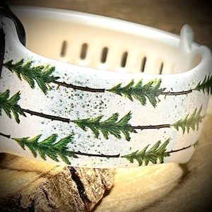 May include: White watch band with a green pine tree pattern. The band has a textured surface and is made of silicone.
