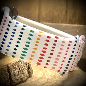 May include: A white watch band with a rainbow polka dot pattern. The band is made of silicone and has a smooth finish.