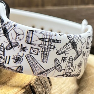 May include: White watch band with a black and white print of airplanes. The print is a repeating pattern of different types of airplanes.