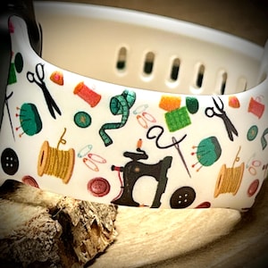 May include: White silicone watch band with a colorful sewing themed pattern. The pattern includes sewing needles, thread spools, scissors, buttons, and a sewing machine.