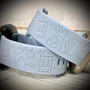 May include: A light blue silicone watch band featuring embossed medical imagery including skeletal structures, a hand X-ray, radiation warning symbols, and broken bones, with the text Rad Tech repeated across the surface of the band.