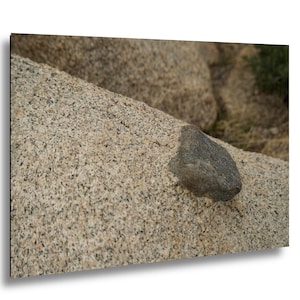 Könnte beinhalten: Nahaufnahme einer großen, strukturierten Felsformation mit einem kleinen, dunkelgrauen Felsen darauf. Der Hauptfelsen hat ein gesprenkeltes, beige-graues Aussehen mit einer rauen, unebenen Textur. Das Bild fängt die natürlichen Details des Steins ein.