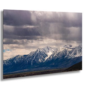 May include: A landscape photograph of a mountain range under a cloudy sky. The mountain peaks are covered in snow, and the sky is filled with dark, ominous clouds. The scene evokes a sense of the natural world.