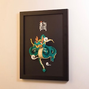 Könnte beinhalten: Ein gerahmtes Schwarzweiß-Pixelbild eines grünen Drachen mit gelben Akzenten. Das chinesische Schriftzeichen für "Drache" ist in Weiß über dem Drachen geschrieben.