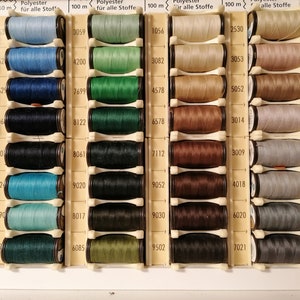 May include: A close-up of a variety of spools of thread in different colors, including pink, red, blue, green, brown, and gray. The spools are arranged in rows and columns, and each spool has a label with a number on it. The labels also indicate that the thread is polyester and suitable for all fabrics. The spools are 100 meters long.