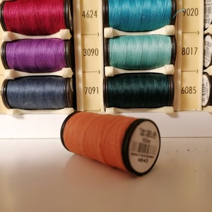May include: A close-up of a single orange spool of thread lying on a white surface. The spool is labeled "7020" and "4643".