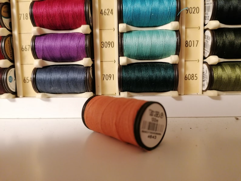 May include: A close-up of a single orange spool of thread lying on a white surface. The spool is labeled "7020" and "4643".