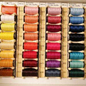 May include: A close-up of a box of 100-meter spools of polyester thread in various colors. The spools are arranged in rows and columns, with each spool labeled with a number.