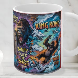 May include: White ceramic mug featuring a colorful graffiti-style design with King Kong imagery. The design includes a large gorilla, airplanes, and the phrases "King Kong," "Beauty Killed the Beast," and "Tragic End."