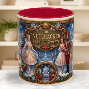 May include: A ceramic mug with a red interior and rim, featuring a festive illustration of The Nutcracker Land of Sweets. The design includes two ballet dancers, a nutcracker soldier, a throne, and winter scenery with gold ornate frames.
