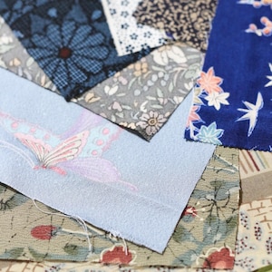 以下が含まれることがあります： さまざまな柄と色の生地見本をクローズアップ。生地には、青、グレー、クリーム色を基調とした花柄、幾何学模様、抽象的なデザインが含まれています。1つの見本には蝶が描かれています。