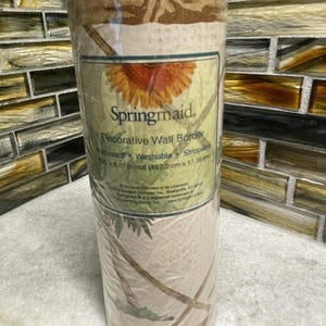 May include: A roll of Springmaid decorative wall border. The label shows a gerbera daisy illustration. The roll is wrapped in clear plastic. The text on the label reads: Prepasted, Washable, Strippable. The roll measures 15 ft x 6.67 in.
