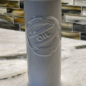 Puede incluir: Dispensador de aceite de cerámica blanca con un diseño circular en relieve que dice "Aceite de oliva" en una fuente de escritura cursiva.