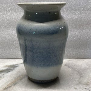 Puede incluir: Un jarrón de cerámica blanco con un esmalte azul. El jarrón tiene un cuerpo redondeado y una abertura acampanada.