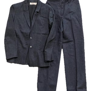 May include: A dark gray two-piece suit. The suit includes a blazer with a notched lapel and two buttons, and matching straight-leg trousers. The blazer has a label inside the collar. The suit is made of a textured fabric.