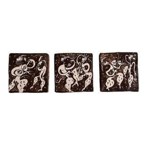 May include: Three square ceramic tiles featuring dark brown backgrounds with cream-colored line art illustrations of stylized figures playing musical instruments. Each tile depicts different musicians in motion, showcasing detailed patterns and fluid shapes.