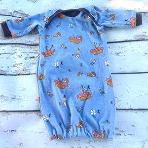 May include: A blue baby gown with a brown trim and a pattern of bears in picnic baskets, bees, and flowers.