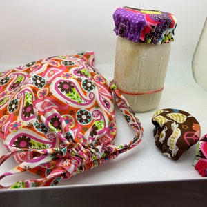 Op de afbeelding: Een set van drie kleurrijke stoffen deksels voor potten. De deksels zijn gemaakt van een gepatenteerde stof met roze, bruine en groene kleuren. De deksels zijn ontworpen om over de bovenkant van potten te passen om voedsel vers te houden.