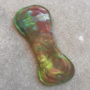 May include: A green, brown, and yellow tie-dye reusable cloth pad with a green stitched edge.