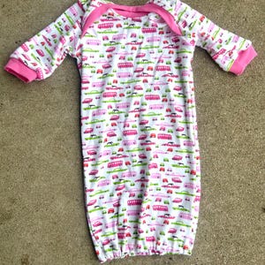 May include: White baby gown with a pink trim and a pattern of pink, green and black cars and buses.