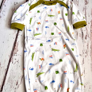 May include: White baby sleepsuit with a green, blue and orange alligator and turtle print. The sleepsuit has green trim around the neck and sleeves. The text "later gator" is repeated on the sleepsuit.