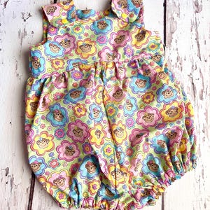 May include: A light green baby onesie with a monkey and flower pattern. The onesie has a ruffled collar and is sleeveless.