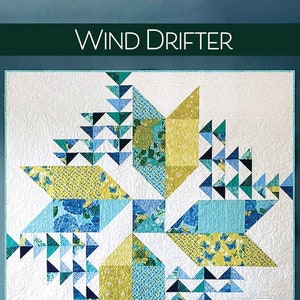 May include: A quilt pattern called "Wind Drifter" by Robin Pickens Quilt Patterns. The quilt is made with a variety of blue, green, and yellow fabrics and features a geometric design. The quilt is displayed on a blue wall with a white chair and a stack of fabric squares.