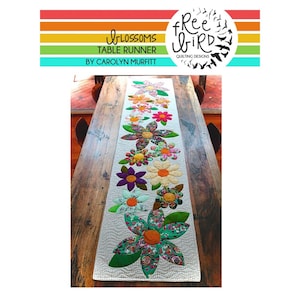 May include: A floral table runner with a quilted design featuring large, colorful flower appliqués. The runner is white with a wavy pattern and is displayed on a wooden table. The top of the image has text that reads "Blossoms Table Runner by Carolyn Murfitt."