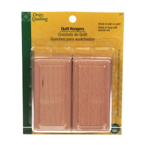 May include: Package of two wooden quilt hangers. The hangers are rectangular with a light brown finish. The packaging includes the text "Quilt Hangers" and "Ready to stain or paint."