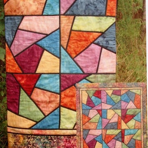 May include: A vibrant quilt with a geometric pattern in shades of orange, pink, blue, green, and purple, outlined in black. A smaller quilt with the same design is also visible. The quilts are likely made of fabric.