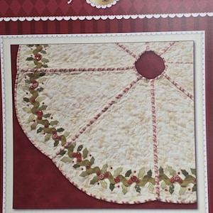 May include: A quilted Christmas tree skirt with a cream-colored background and a holly and berry border. The skirt has a circular design with a center hole and is trimmed with red stitching. The text "Holly & Berries Tree Skirt" is visible.