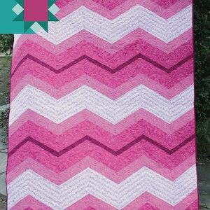 May include: A handmade quilt with a chevron pattern in shades of pink and white. The quilt features the text "Peppermint Stripe" and "Carolina Moore". The quilt is displayed outdoors.