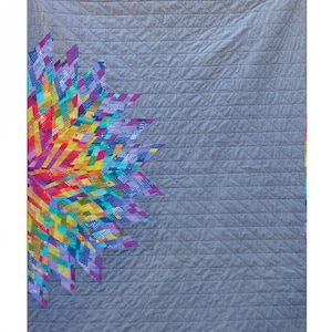 May include: A colourful quilt with a geometric design in shades of pink, purple, blue, green, yellow, and orange. The quilt is 42 inches by 55 inches and is titled "Luminary Quilt" by Jamie Swanson.