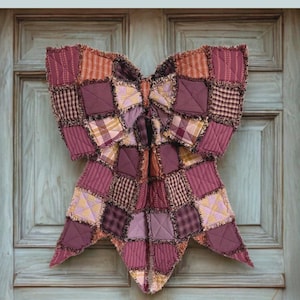 May include: A large bow made of patchwork fabric squares with frayed edges in shades of maroon, plum, and orange. The text reads: THE BIG GIANT RAG QUILT BOW, Designed to be reversible, Charm pack and fat quarter friendly, Simple assembly technique, A beginner-friendly sewing pattern + video tutorial by: LGC LINDSEY GRACE CREATES.